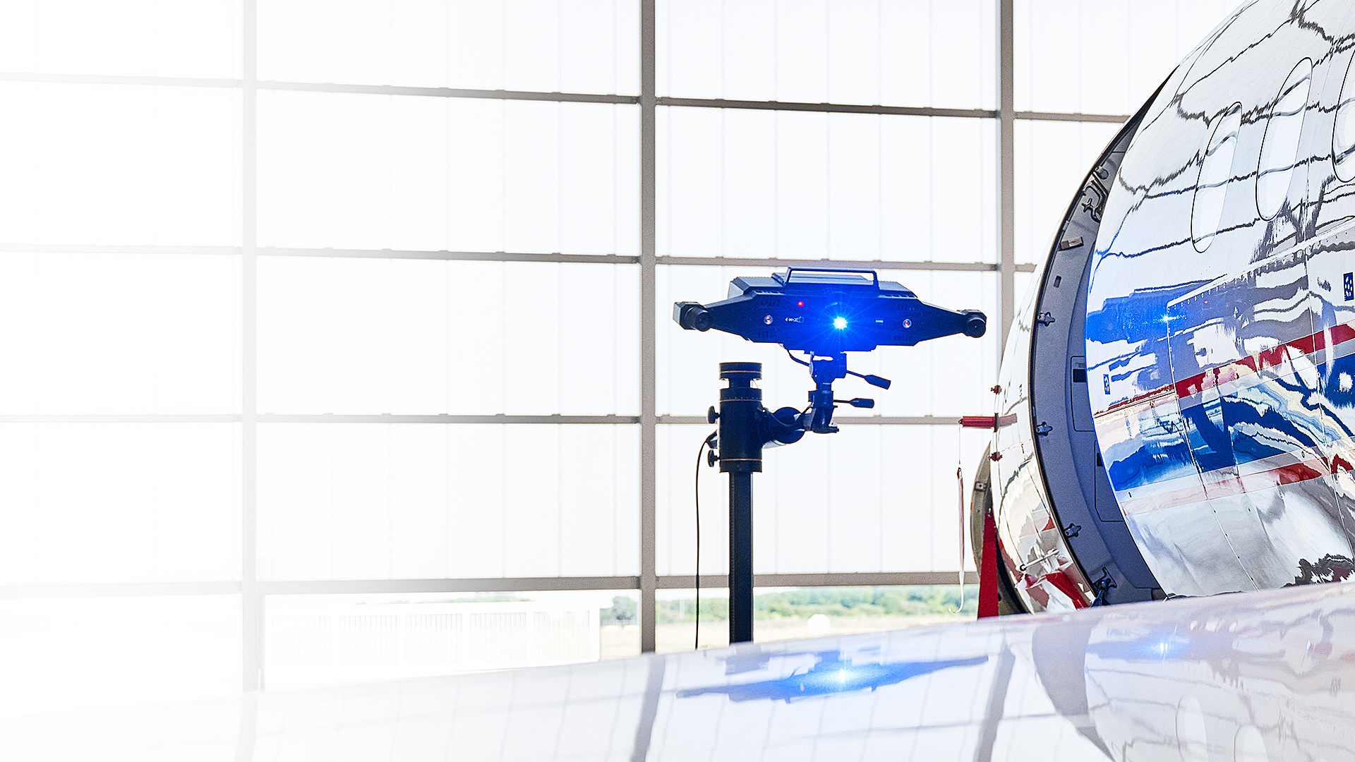 A ZEISS 3D scanning system captures data from the exterior surface of an aircraft inside a brightly lit hangar.