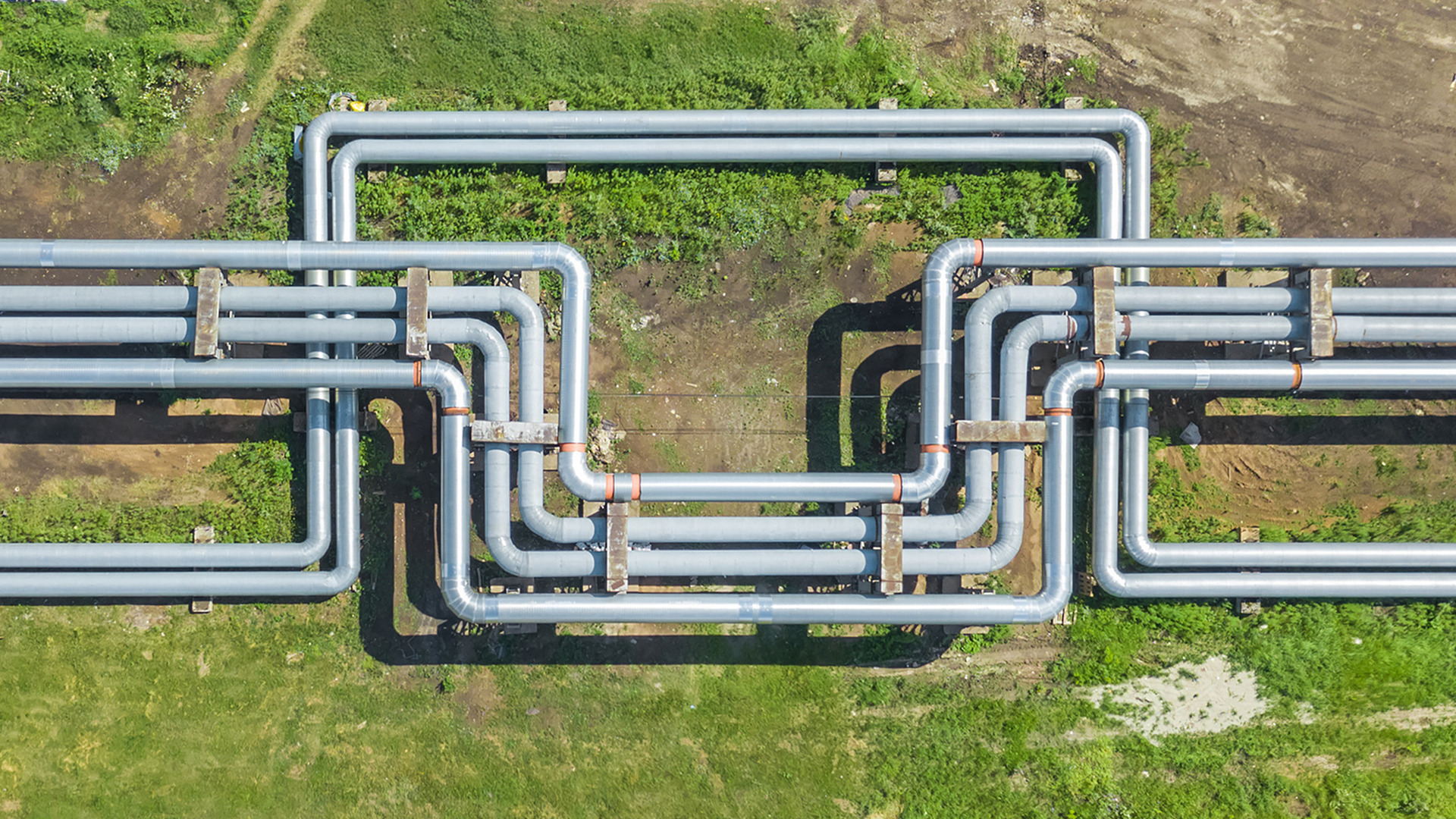 Aerial view of a network of large industrial pipelines running above ground through a grassy area.