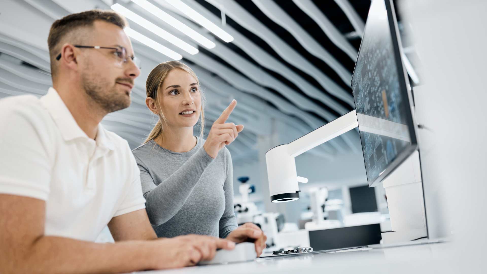 Two professionals are working together in a modern laboratory, analyzing data on a large monitor connected to ZEISS Smartzoom 100.