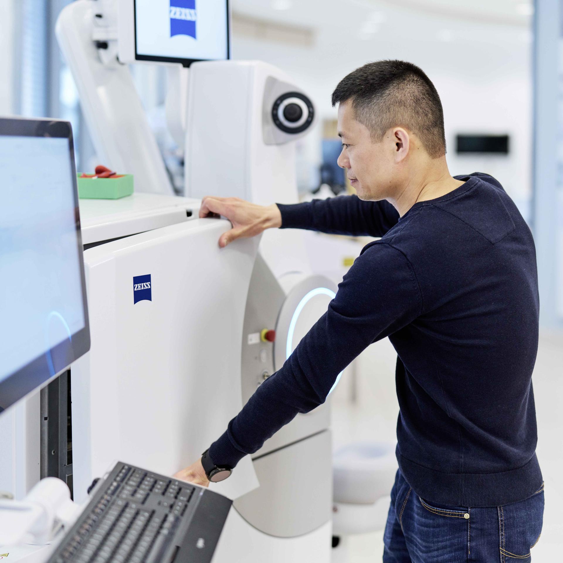 A man operates a high-tech imaging or diagnostic device branded with the ZEISS logo in a modern, clinical environment.