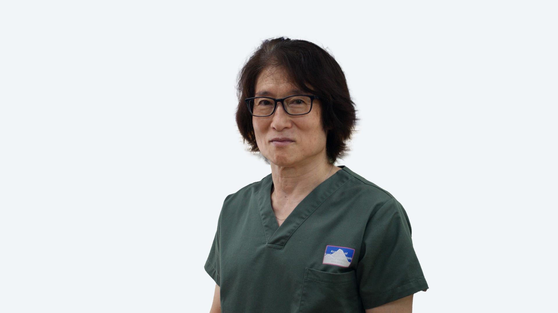 Portrait of a man in green scrubs with glasses, smiling at the camera.