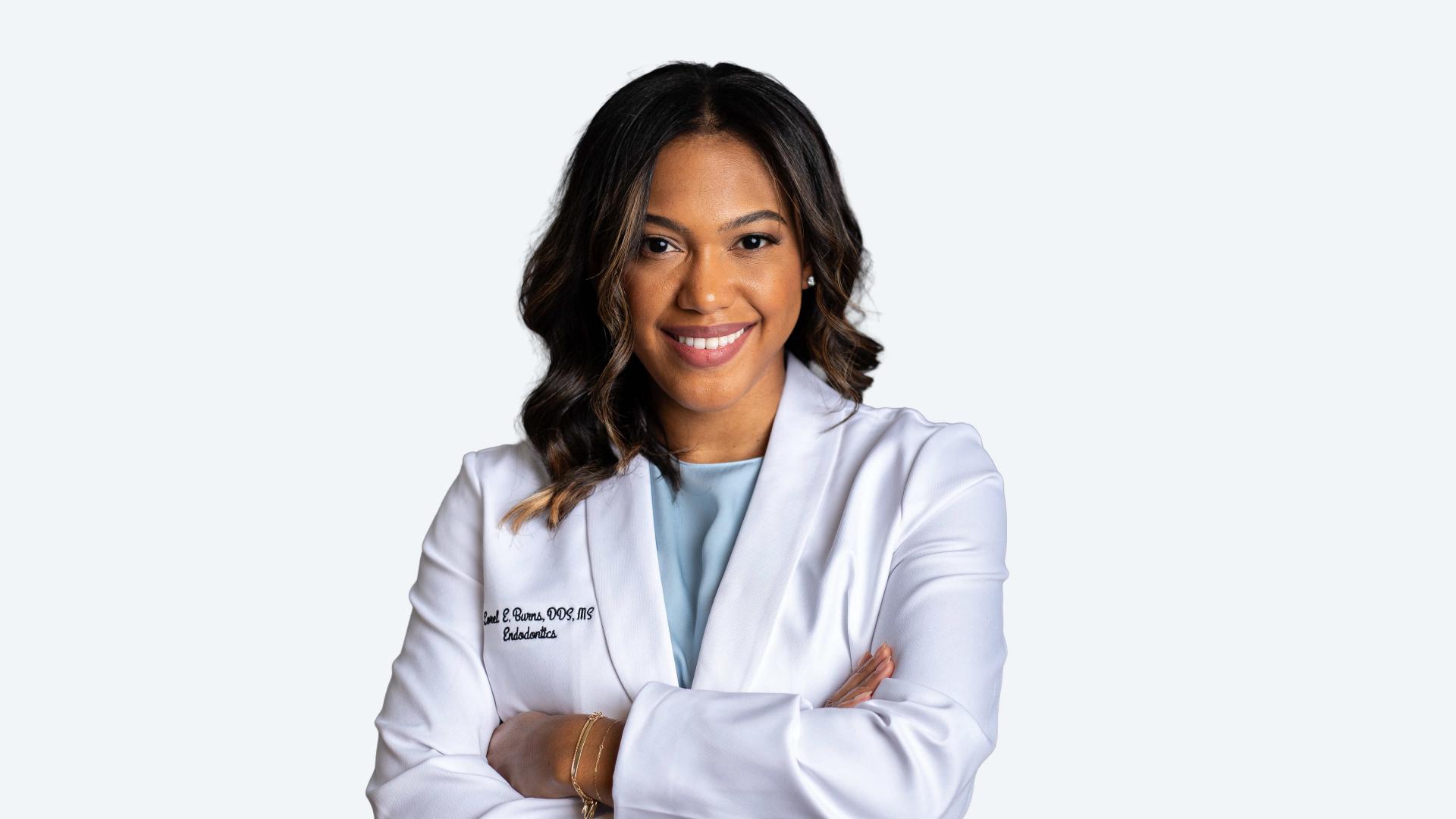 A woman in a white lab coat stands with her arms crossed, exuding confidence and professionalism in a laboratory setting.