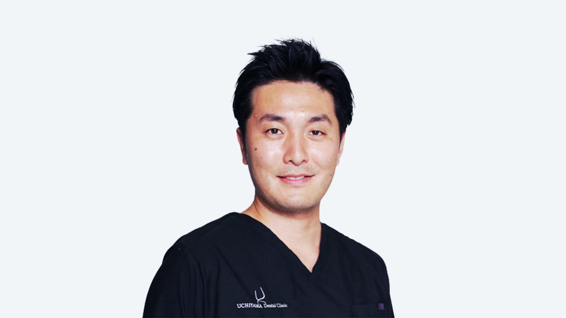 A man wearing a black shirt and scrub pants stands confidently, showcasing a professional appearance.