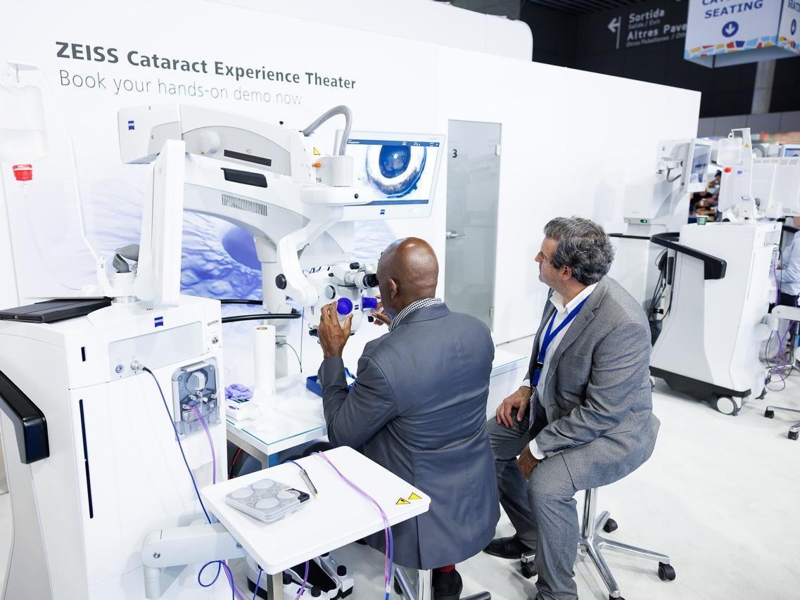 Two men in suits interact with advanced ophthalmic equipment at the ZEISS Cataract Experience Theater demonstration area.