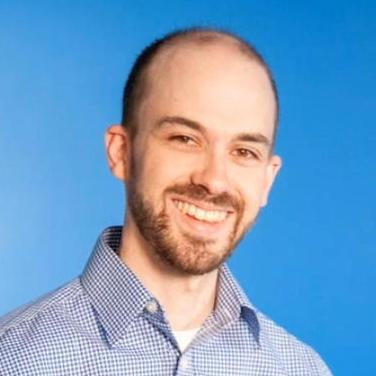 Smiling man wearing a checkered shirt standing in front of a solid blue background.
