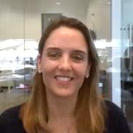 A woman is smiling in a modern office setting with glass walls, featuring a visible ZEISS examination room in the background.