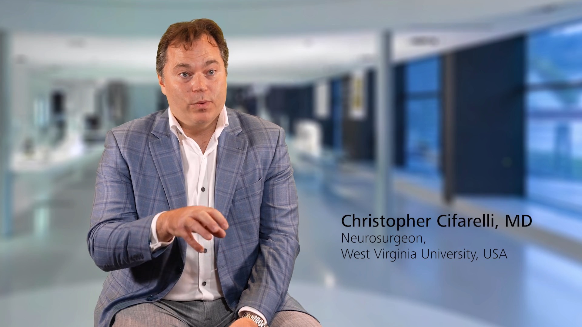 Christopher Cifarelli, MD, Neurosurgeon at West Virginia University, USA, is sitting in a modern medical facility; background features a blurred clinical environment with ZEISS branding context.