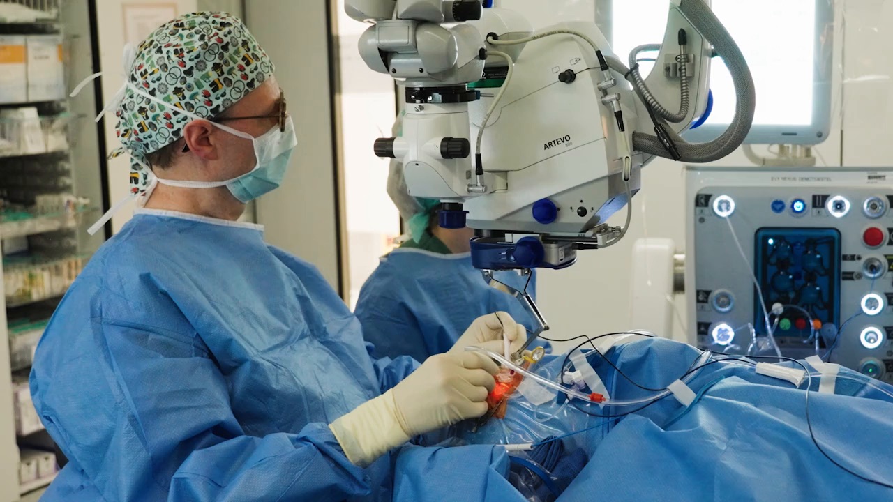 Professor Peter Stalmans performing a procedure using a ZEISS surgical microscope in a sterile operating room environment.