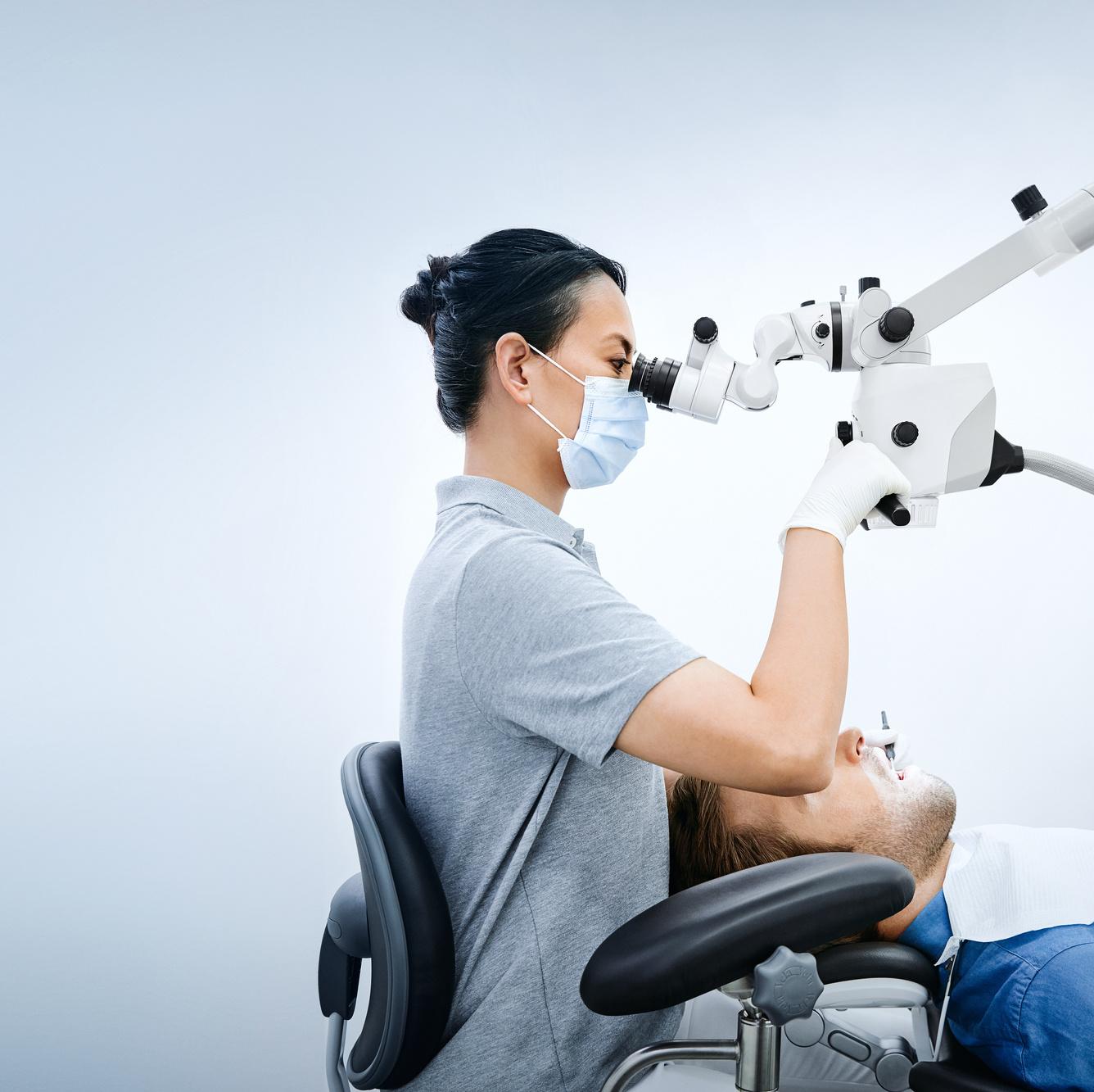 A dental professional uses a ZEISS surgical microscope while examining a patient in a dental clinic.
