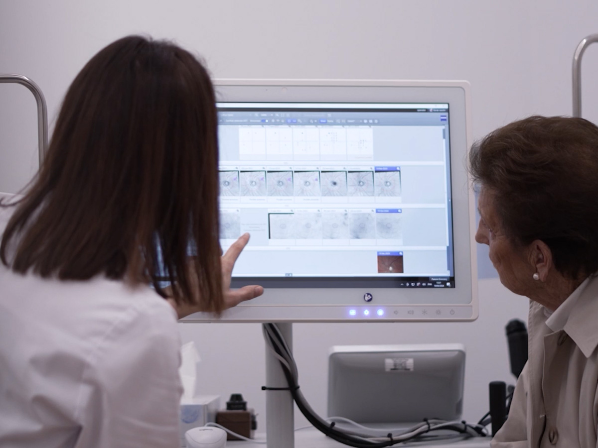 A medical professional shows an elderly patient diagnostic images on a computer screen in a clinical setting.