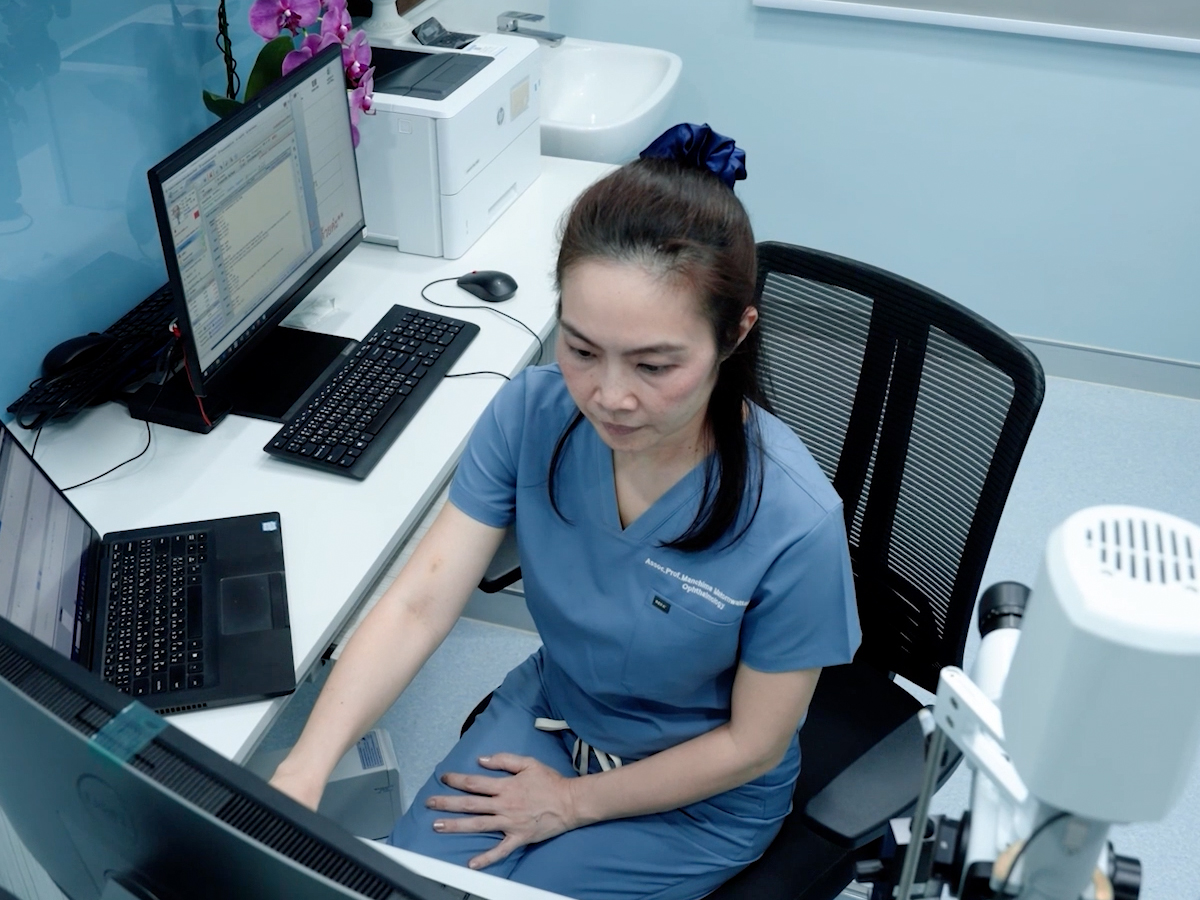 A medical professional in scrubs works at a dual-monitor computer station with ZEISS equipment in a clinical setting.