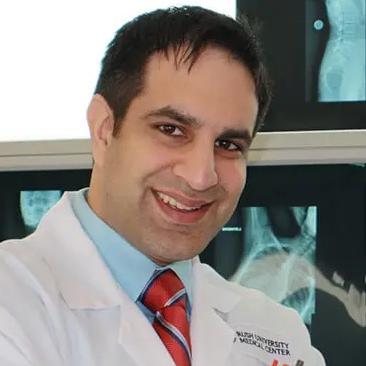 Dr. Neil Badlani in a white lab coat standing in front of X-ray images.