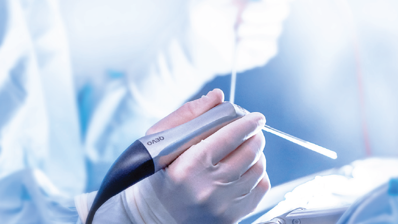A medical professional holds a ZEISS QEVO in a bright, sterile operating room environment.