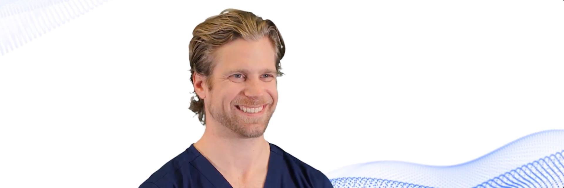 Smiling man in medical scrubs standing in front of a white background with blue wave graphics, representing ZEISS.
