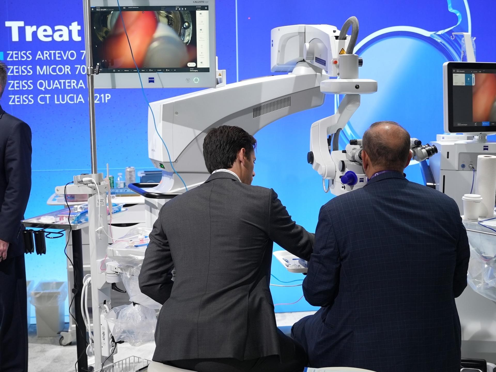 Two men in professional attire examine advanced medical imaging equipment at a ZEISS exhibition booth showcasing cataract workflow solutions.