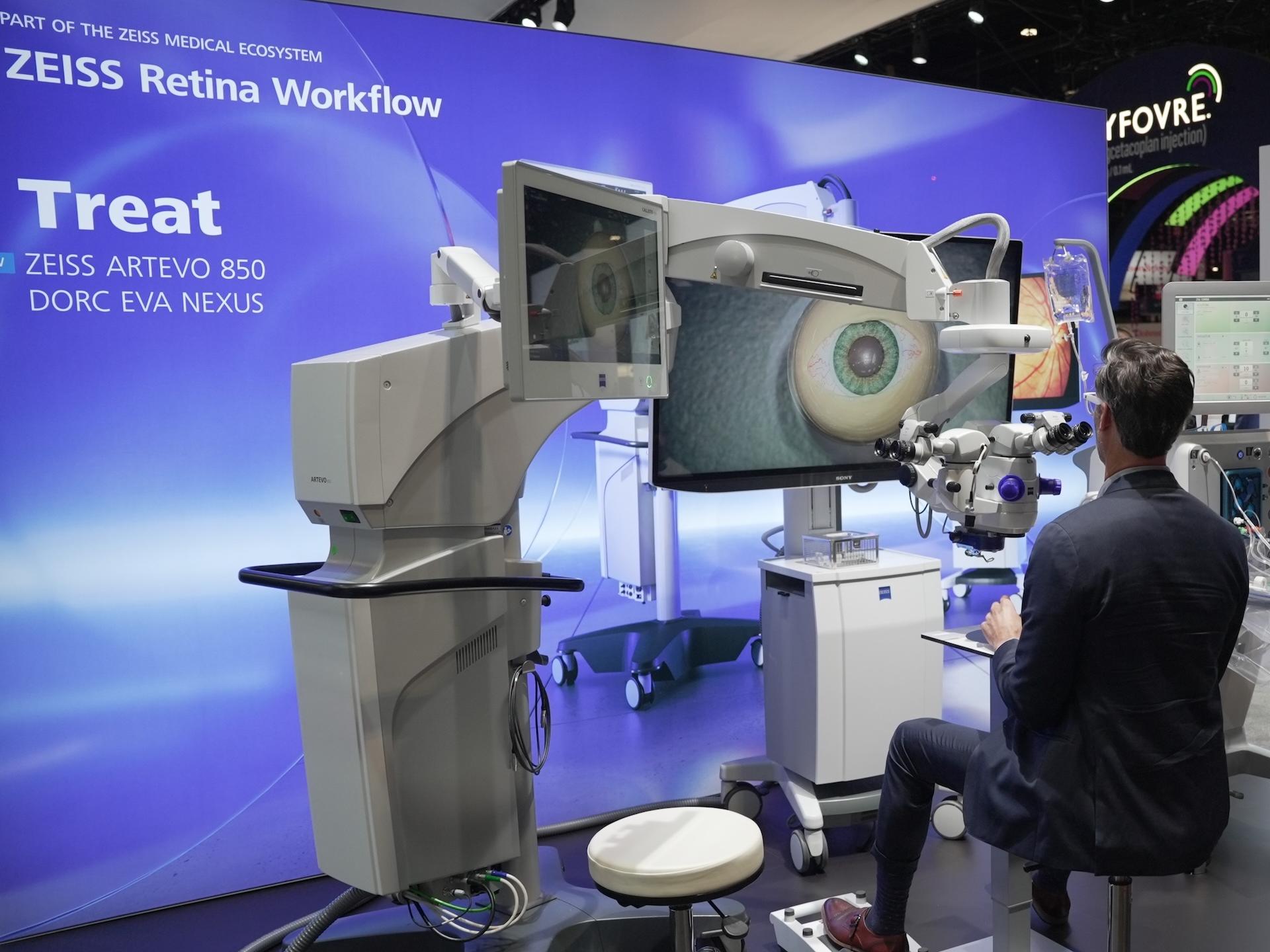A man demonstrates a ZEISS ARTEVO 850 surgical microscope system as part of the ZEISS Retina Workflow setup at a professional exhibition booth.