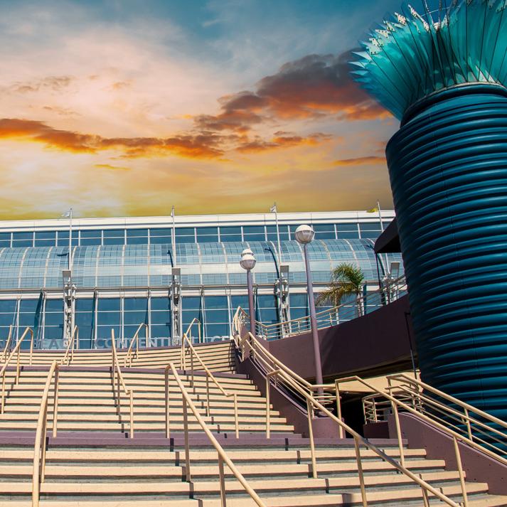 Wide staircase leading up to a modern glass building with two large blue cylindrical structures on either side, set against a dramatic sunset sky.