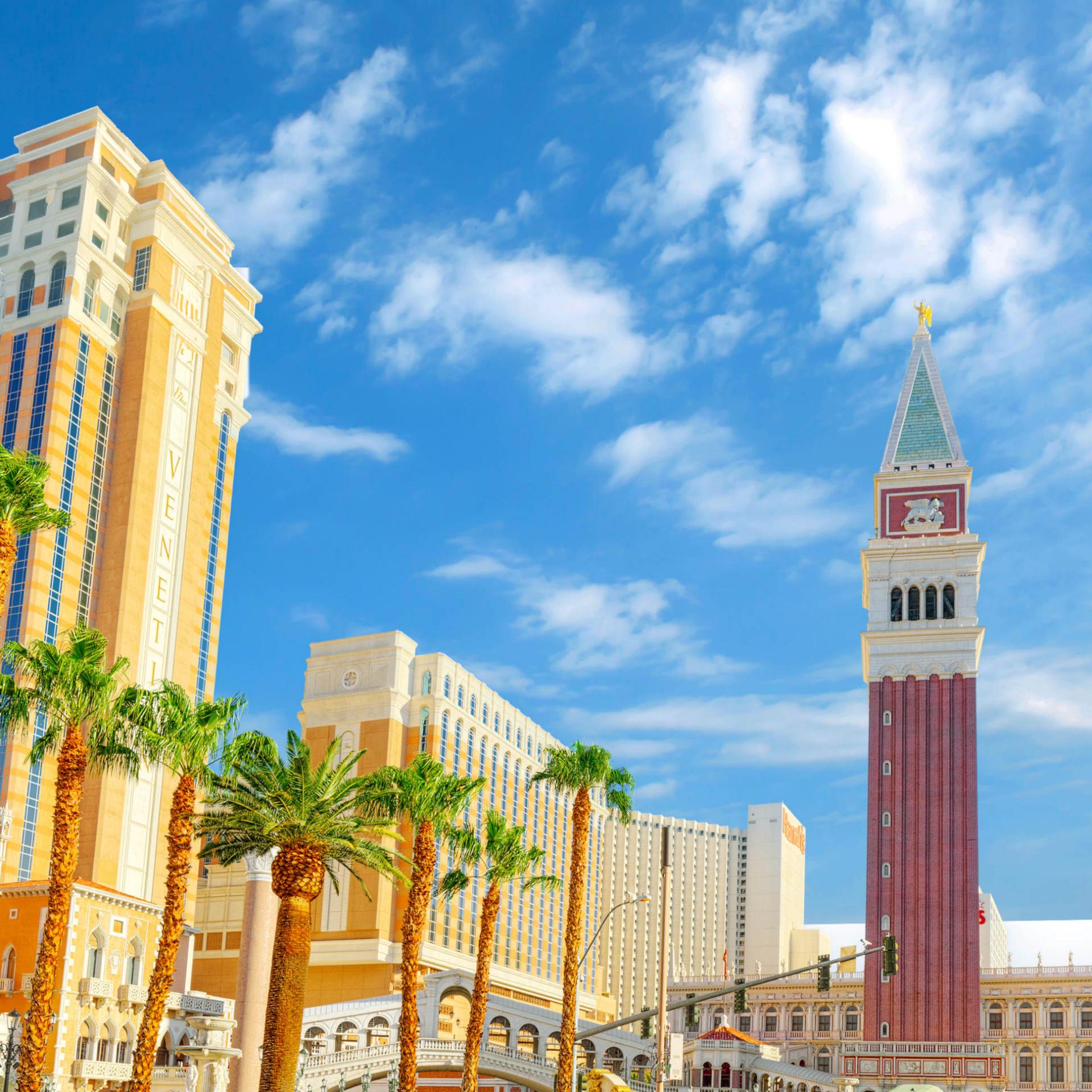 View of the Venetian Hotel and surrounding palm trees under a clear blue sky in Las Vegas.