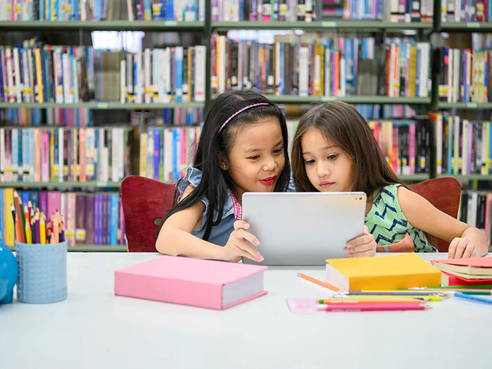 two young girls looking at a tablet happily