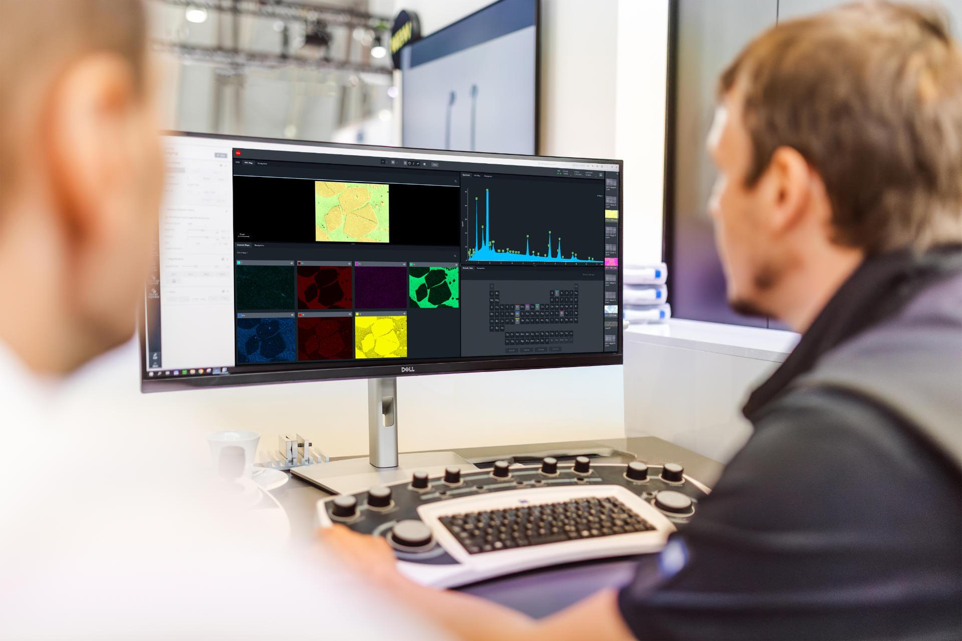 Two people sit in front of a monitor which displays various statistics and other technical diagrams