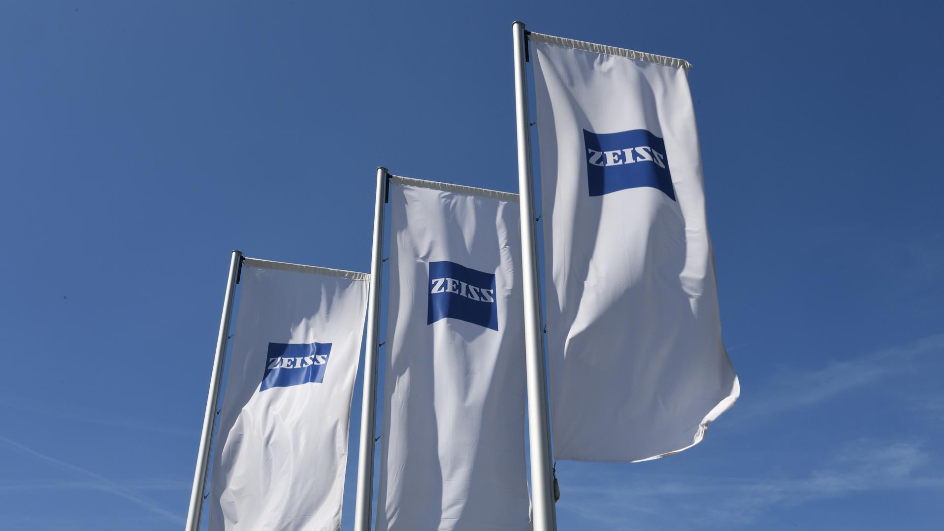 Three white flags with ZEISS logo under blue sky