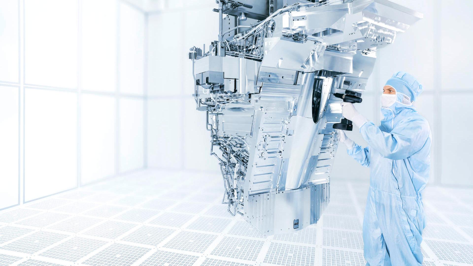 The image shows the ZEISS EUV illumination system in a clean room with a man. The system consists of 15,000 individual parts and weighs 1.5 tons.