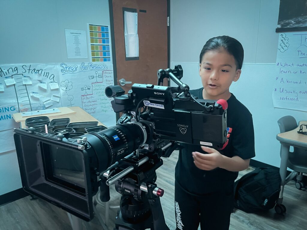 Two people are working with professional film production equipment, including a camera and monitor, in a studio setting featuring ZEISS lenses.