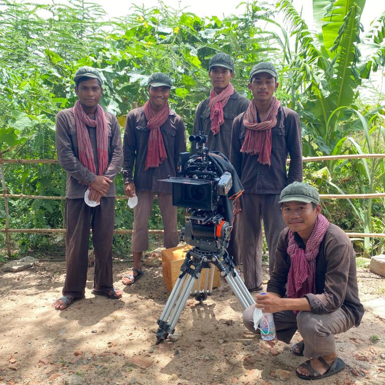 A camera operator films a scene using a professional camera setup equipped with ZEISS lenses in a studio environment.