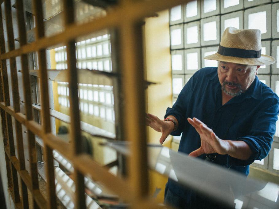 A group of people stands outdoors while a teenage boy reads from a paper as reporters hold microphones toward him.