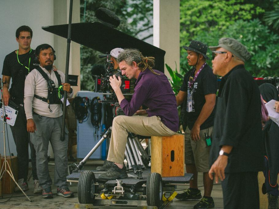 Two people are working with professional film production equipment, including a camera and monitor, in a studio setting featuring ZEISS lenses.