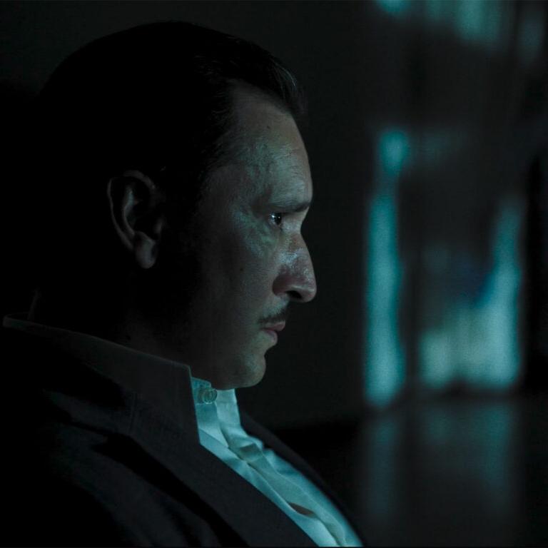 A camera operator films a scene using a professional camera setup equipped with ZEISS lenses in a studio environment.