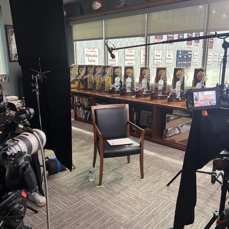 Two people are working with professional film production equipment, including a camera and monitor, in a studio setting featuring ZEISS lenses.