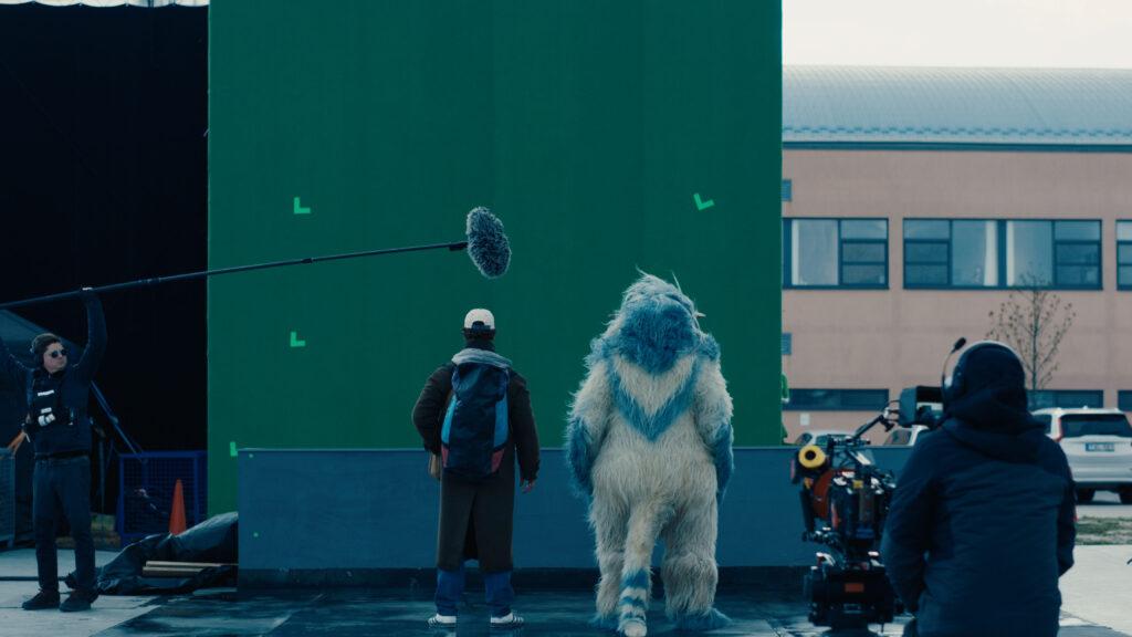 A group of people stands outdoors while a teenage boy reads from a paper as reporters hold microphones toward him.