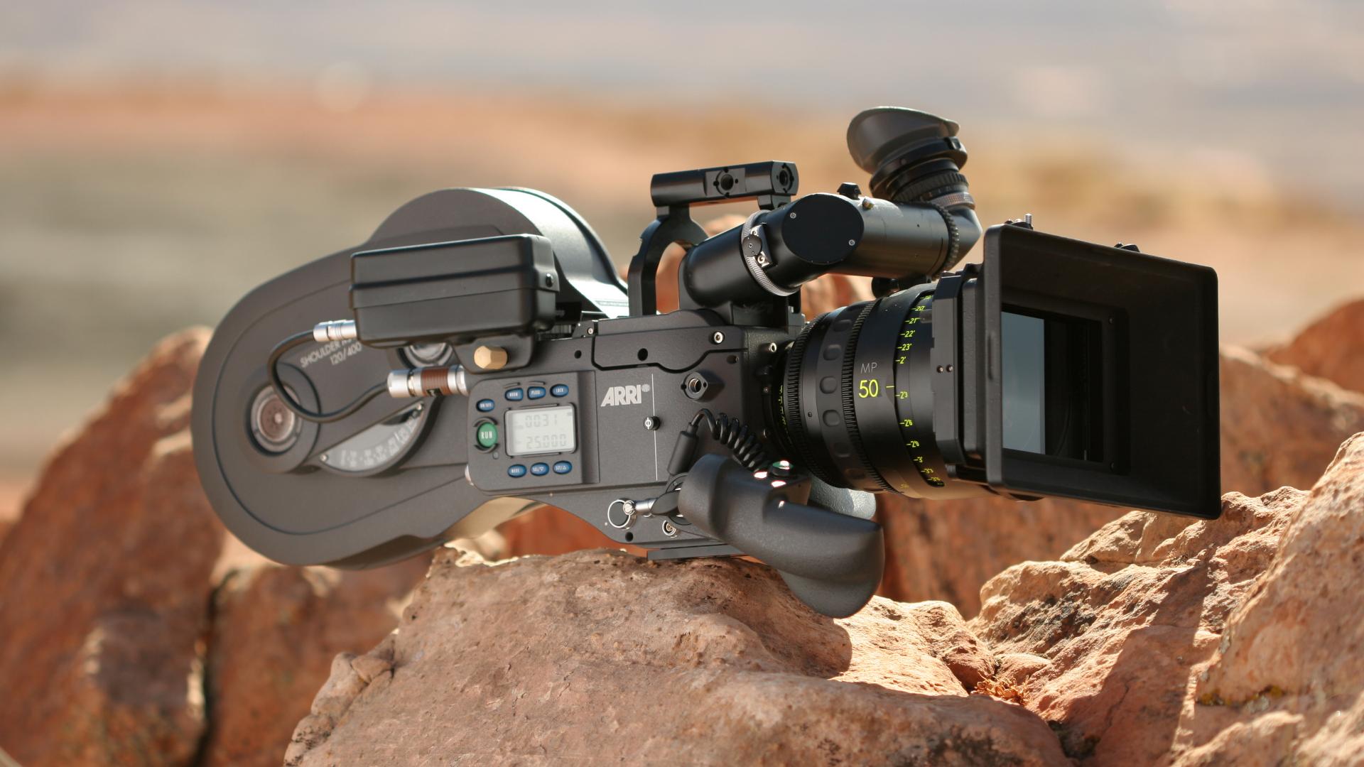 Professional ARRI film camera equipped with a ZEISS lens positioned on rocky terrain in an outdoor setting.