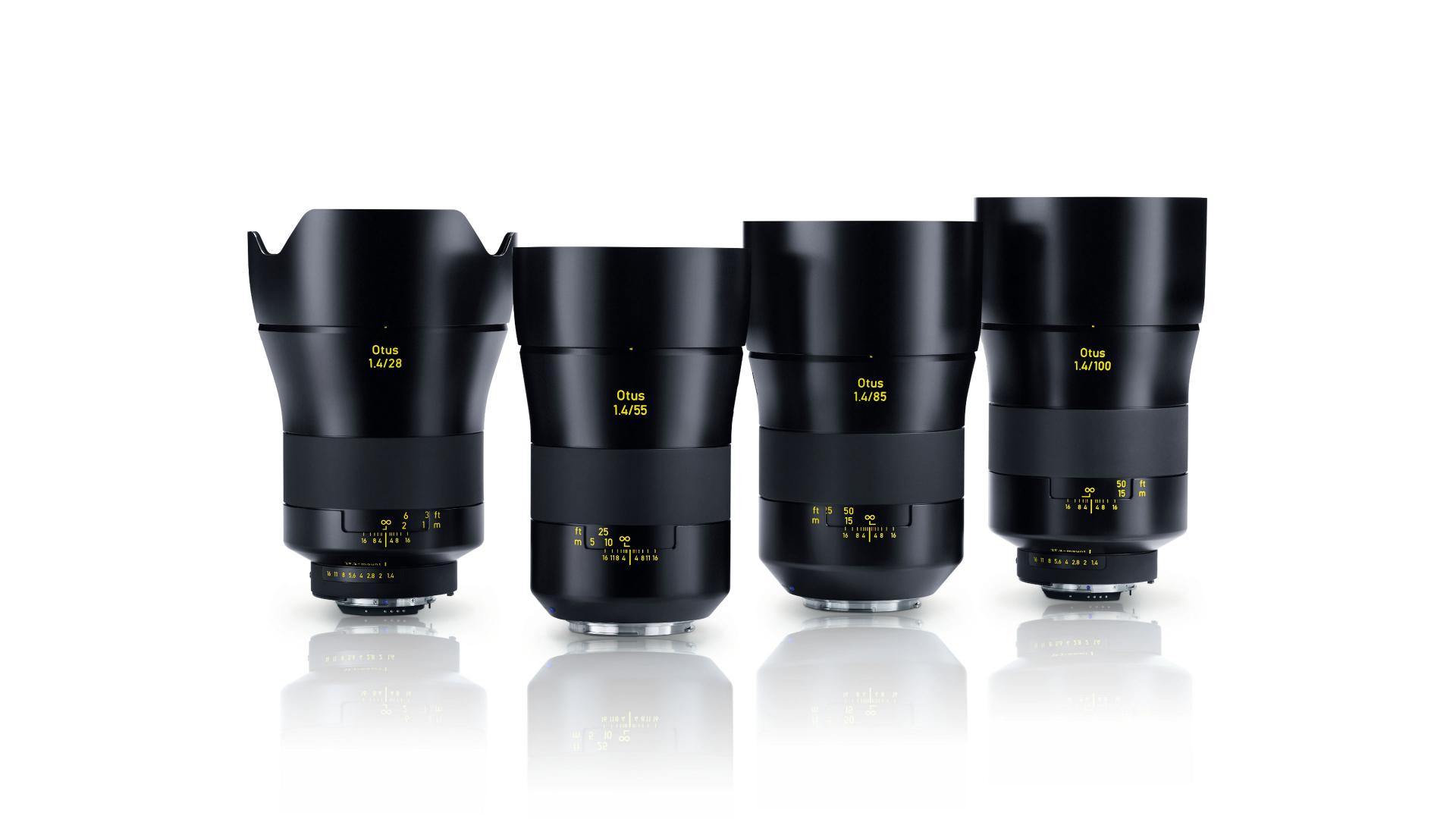 Four ZEISS camera lenses with black metal housings and yellow labeling are displayed upright in a row on a white reflective surface.
