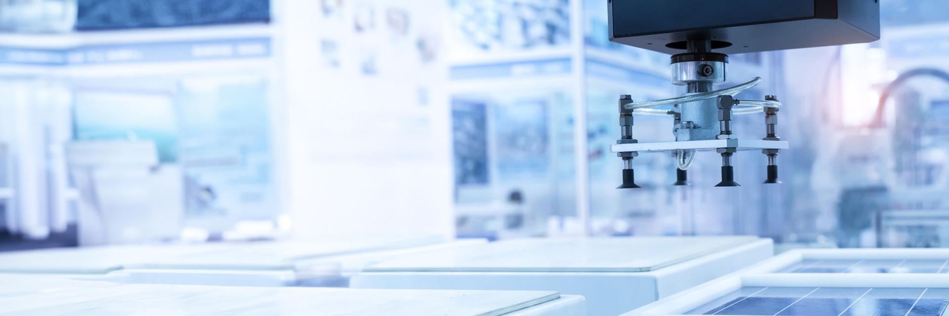 Robotic arm with suction cups operating over glass panels in a high-tech manufacturing facility.