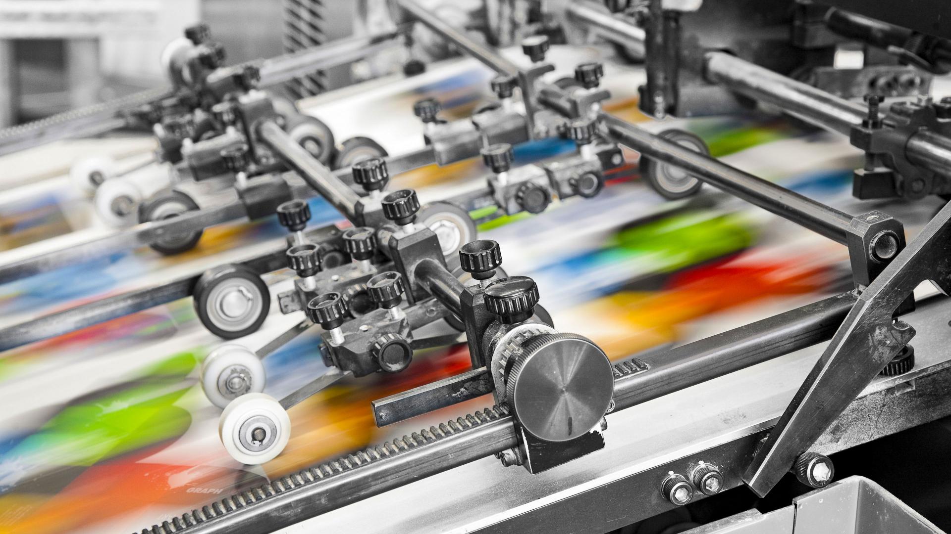 Close-up of an industrial printing press in operation with colorful sheets moving rapidly through the machine.