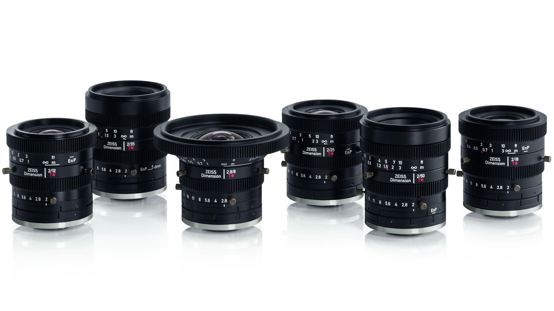 Six ZEISS camera lenses of varying focal lengths are arranged in a row on a reflective white surface.