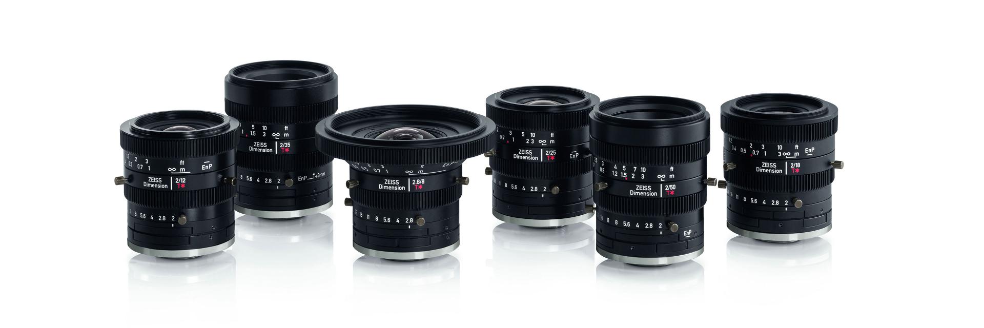Six ZEISS camera lenses of varying focal lengths are arranged in a row on a white reflective surface.