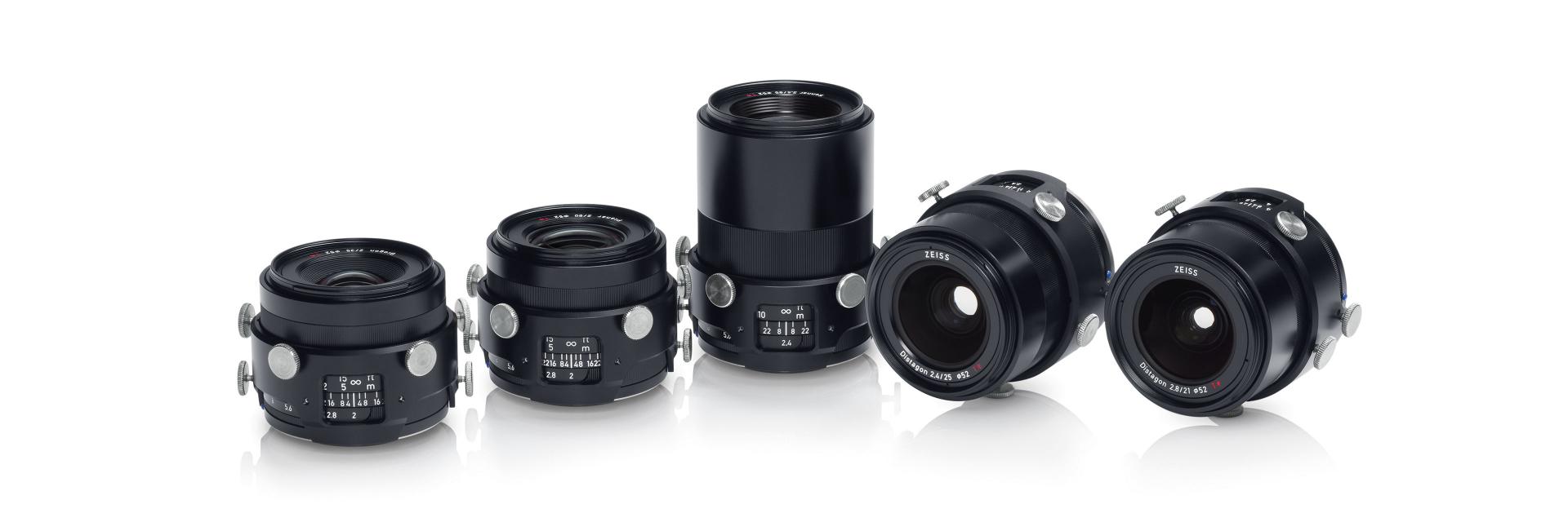 Five professional ZEISS camera lenses are displayed in a row on a white reflective surface.
