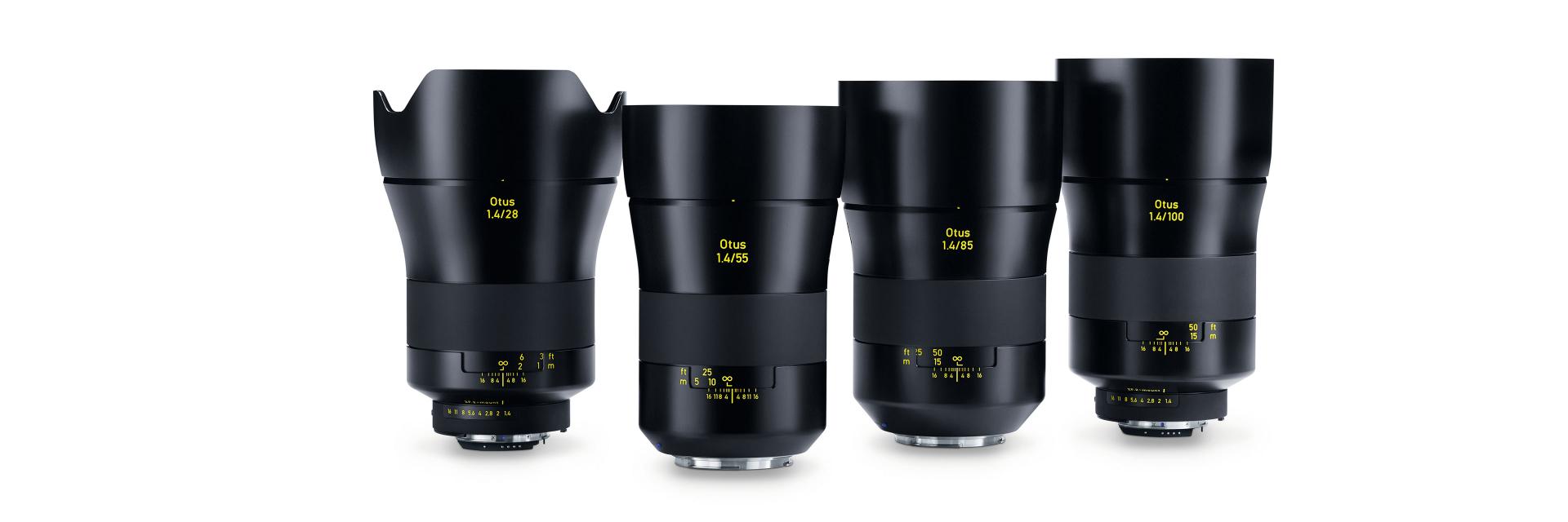 Four ZEISS camera lenses with black metal housings and yellow labeling are displayed upright in a row on a white reflective surface.
