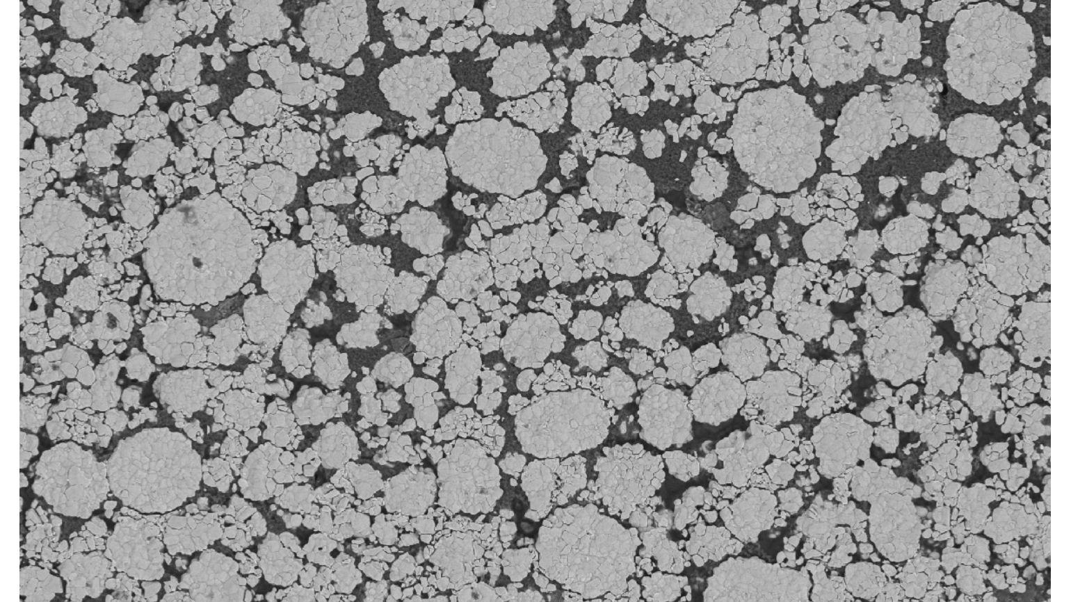 Electron microscopic view of a metallic surface showing a pattern of variously sized circular grains against a darker background.
