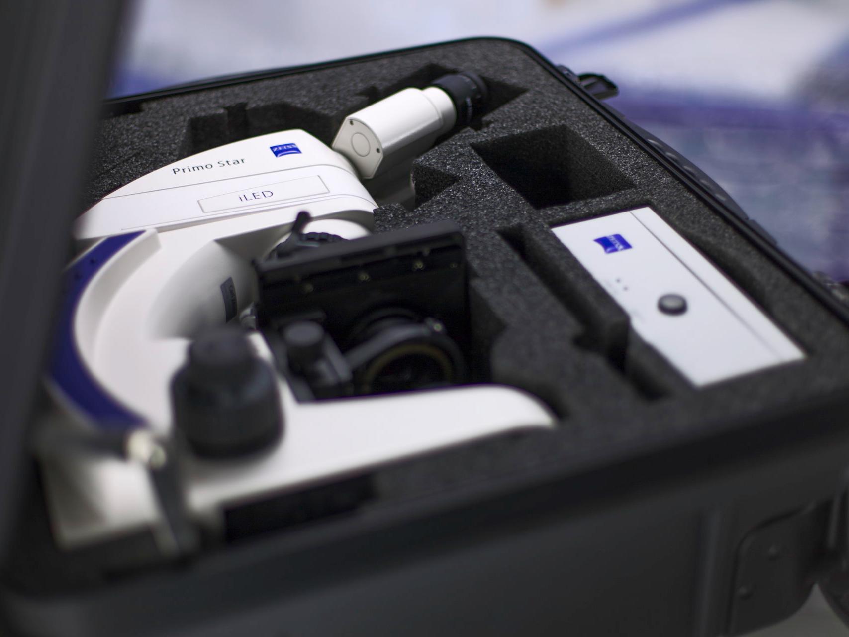 A white ZEISS Primo Star microscope securely packed in a custom foam case, alongside an accessory box, inside a hard-shell carrying case.