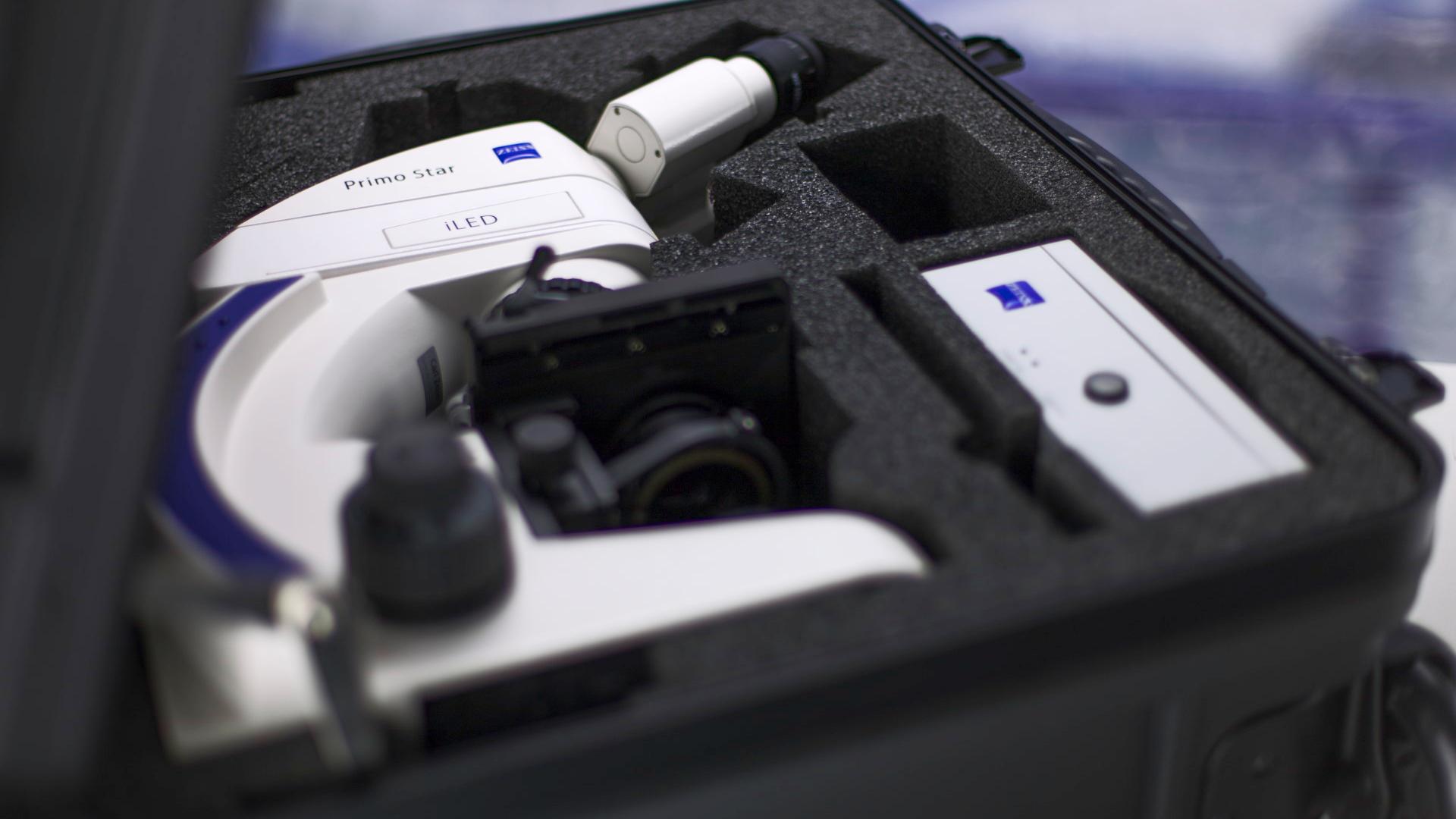 A white ZEISS Primo Star microscope securely packed in a custom foam case, alongside an accessory box, inside a hard-shell carrying case.