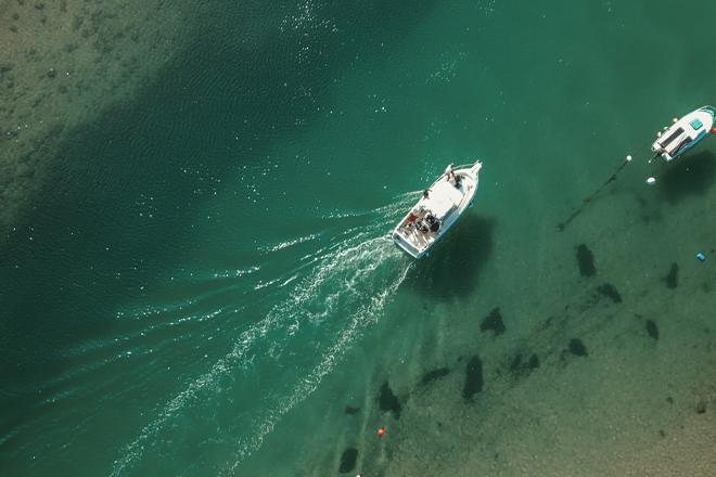 Bird's eye view of a boat in clear water, surrounded by a few kayaks