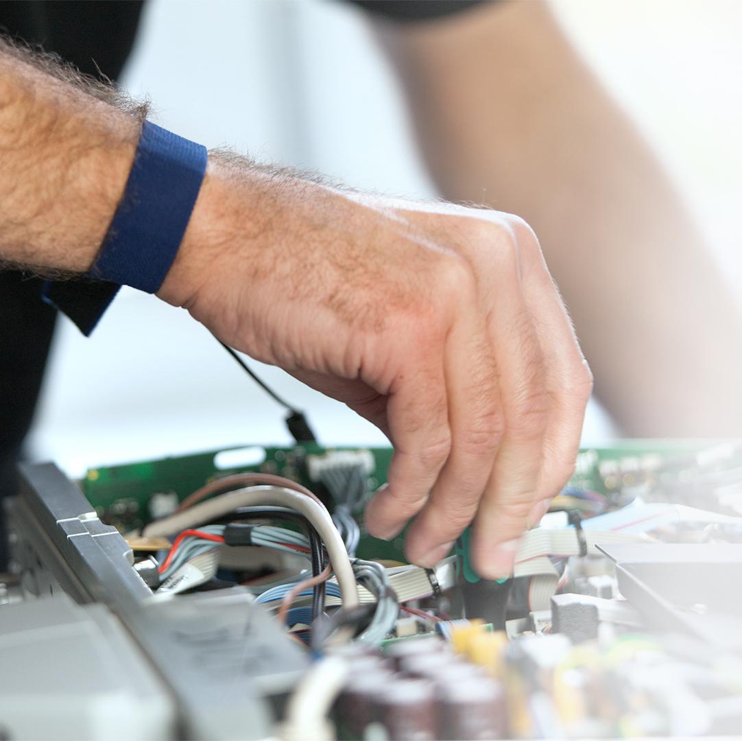 A technician’s hand working on an open electronic circuit with visible wires and components