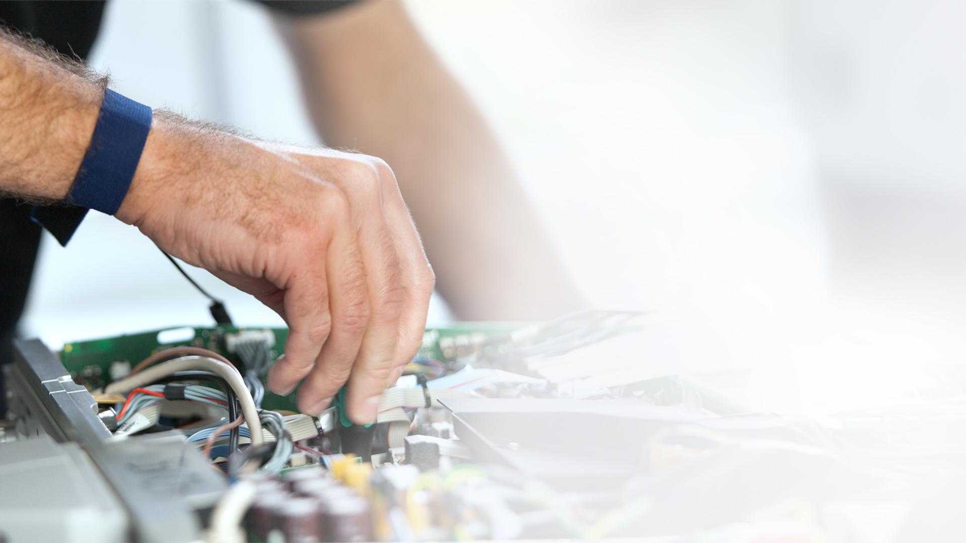 A technician’s hand working on an open electronic circuit with visible wires and components