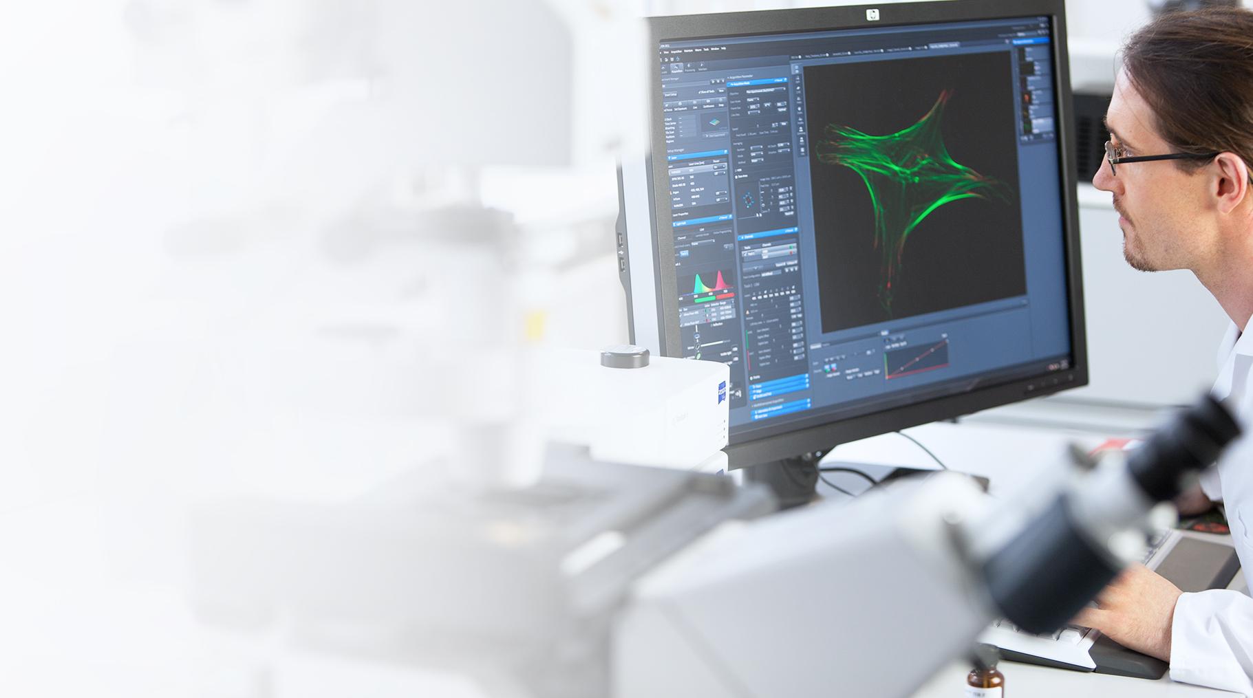 Scientist analyzing microscopic data on a computer screen in a laboratory setting, with a microscope in the foreground