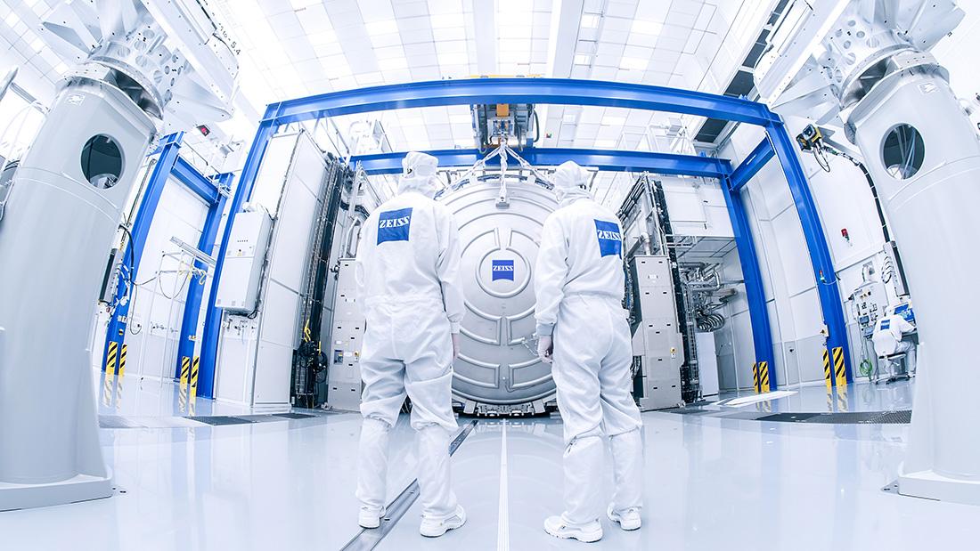 Two employees stand in front of the metrology of the High-NA-EUV lithography in the vacuum chamber of the ZEISS SMT clean room