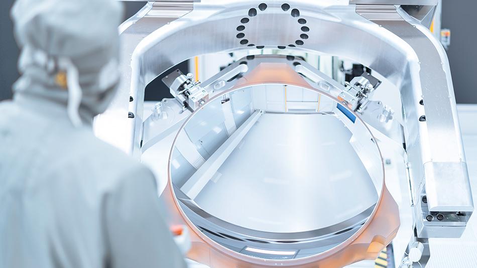 A ZEISS SMT employee stands in front of a mirror of the High-NA-EUV technology in the clean room